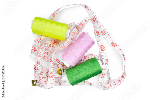 Set of sewing accessories: The white measuring centimetric tape and three bobbins of yellow, green, pink thread isolated on a white background photo