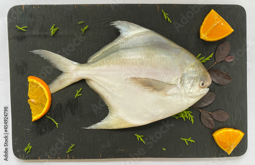 Top view of Silver Pomfret,White Pomfret fish dish cooking with various ingredients. Fresh raw fish decorated on a wooden pad, white background.Selective focus. photo