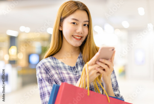 Smiling young Asian woman with shopping colour bags over mall background. using a smart phone shopping online and smiling while standing mall building. lifestyle concept