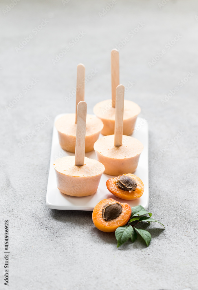 Mini apricot ice cream on a wooden stick on a ceramic plate on a light background Mini apricot ice cream on a wooden stick on a ceramic plate on a light background