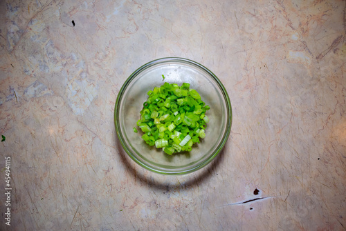 finely cut green onions in a glass bowl on a light pink table
