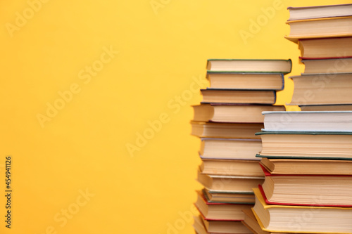 Many hardcover books on orange background  space for text. Library material
