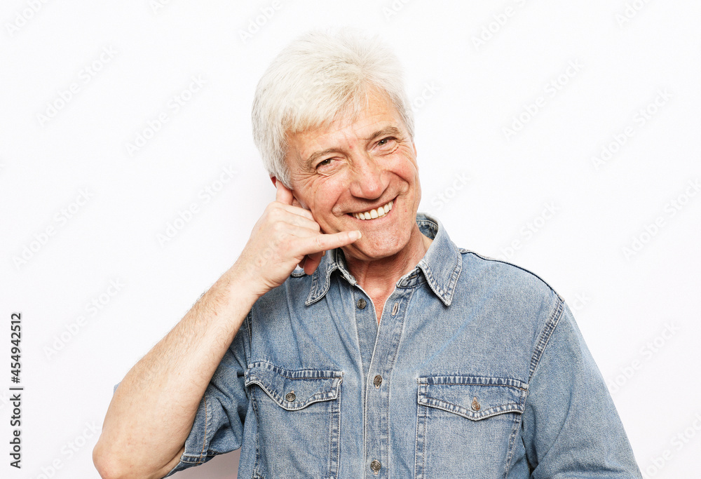 Photo of aged man happy positive smile show finger call phone sign over white background. Photo of aged man happy positive smile show finger call phone sign over white background.