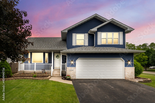 Photography Exterior of a suburban home with blue siding, a white front porch, and white shutters at sunset