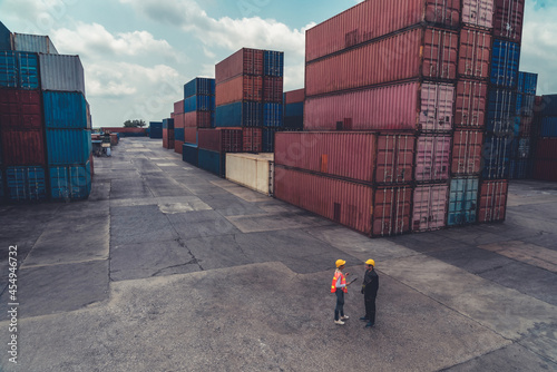 Industrial worker works with co-worker at overseas shipping container yard . Logistics supply chain management and international goods export concept .