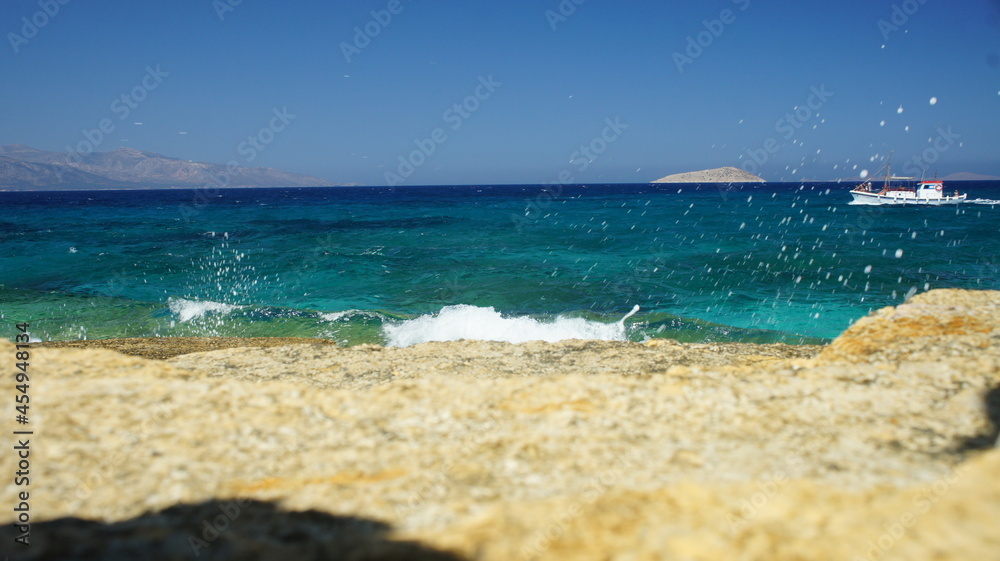 Sea and sky as a wave splash appears on the cliff in the Greek island of koufonisi August 2021
