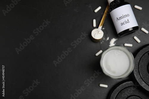 Amino acid shake, powder, pills and weight plates on black background, flat lay. Space for text