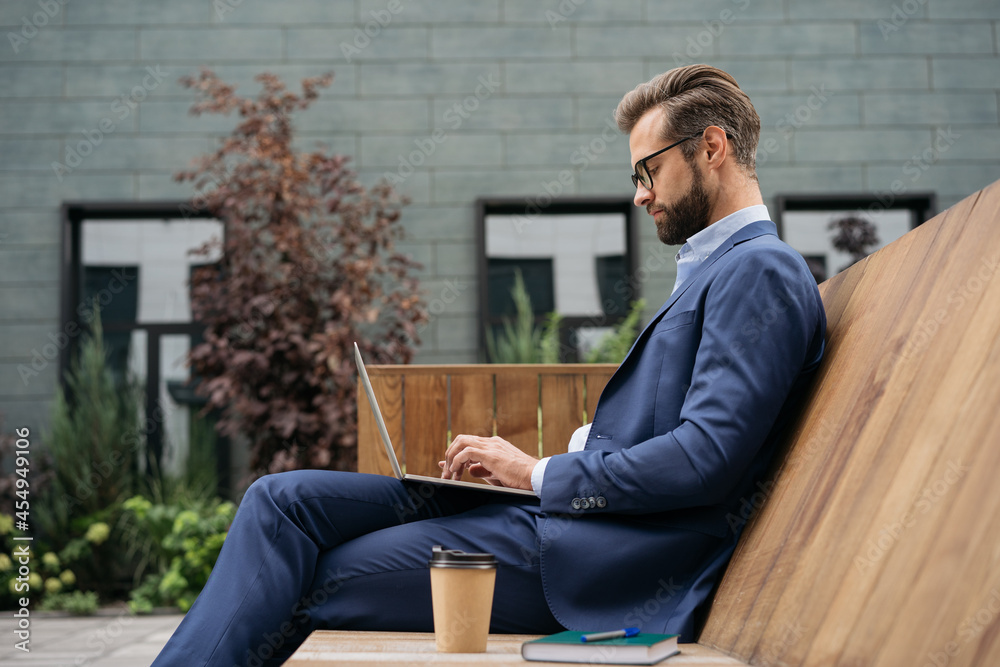 Handsome businessman using laptop computer, searching online, watching training courses sitting at workplace. Young bearded manager wearing stylish suit and eyeglasses typing, working project Handsome businessman using laptop computer, searching online, watching training courses sitting at workplace. Young bearded manager wearing stylish suit and eyeglasses typing, working project