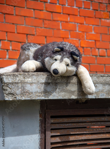 A huge toy dog is lying against a brick wall on the street.