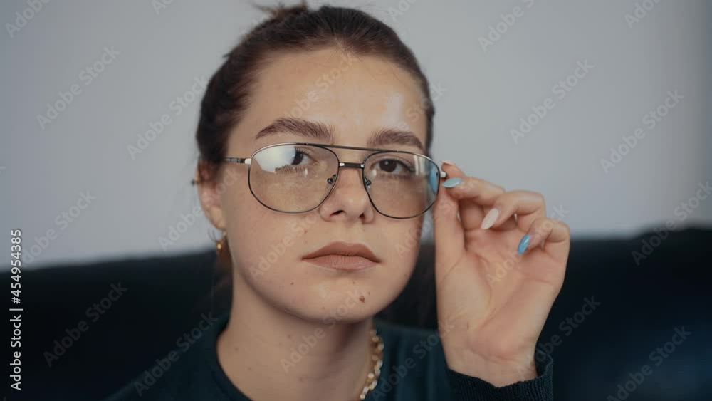 Close-up of the freckled, red-haired young woman with glasses holding her hand near her eyes. Dressed in a dark green blouse, sitting on a black sofa, at home. The concept of the woman relaxing at Close-up of the freckled, red-haired young woman with glasses holding her hand near her eyes. Dressed in a dark green blouse, sitting on a black sofa, at home. The concept of the woman relaxing at