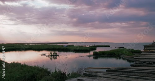 Scenic purple sunrise over lake and wetland with old wooden pier, idyllic nature static shot. National park of Delta Axios river, Greece. photo