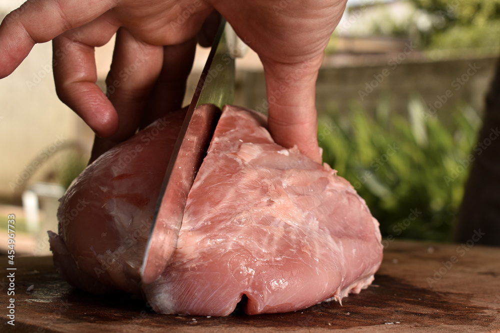 close up de manos de hombre cortando un trozo de carne cruda de cerdo