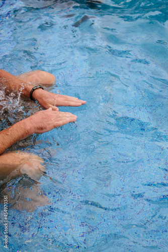 Man's hands touches the clear blue water in the pool. Summer day in the pool party.