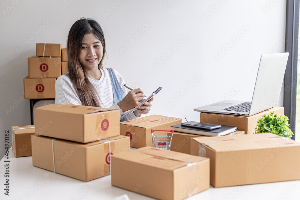 Woman holding parcel boxes to write customer address information before shipping to customers via private transport service, she works online, she sells through website. Online selling concept. Woman holding parcel boxes to write customer address information before shipping to customers via private transport service, she works online, she sells through website. Online selling concept.