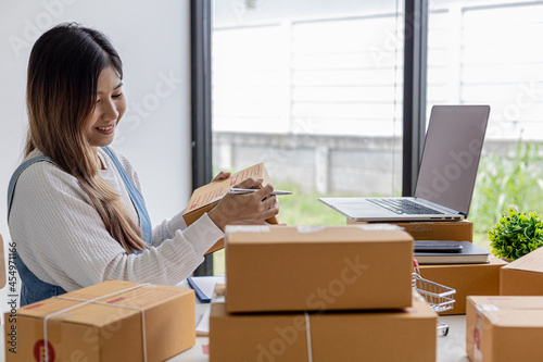 Woman holding parcel boxes to write customer address information before shipping to customers via private transport service, she works online, she sells through website. Online selling concept.