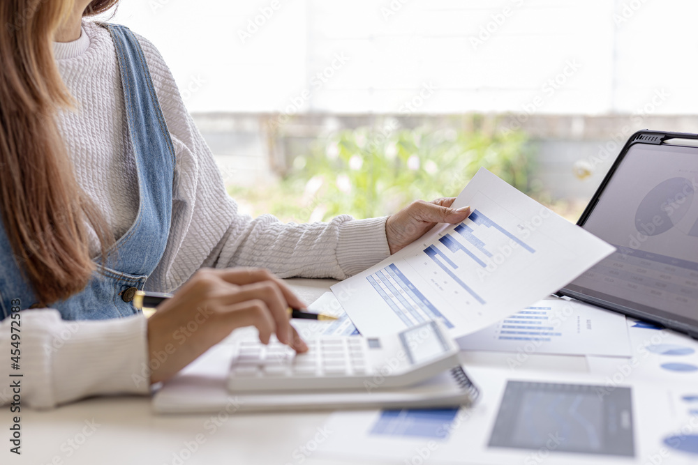 Fototapeta premium Woman holding a document and pressing a white calculator on her desk, an auditor is reviewing company bookkeeping data to verify validity and fraud, accounting manipulation. Audit concept.