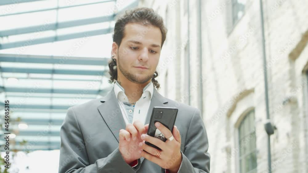 A young successful businessman is working outdoor using smartphone. Man in a casual wear. Business, freelance and remote work. A young successful businessman is working outdoor using smartphone. Man in a casual wear. Business, freelance and remote work.