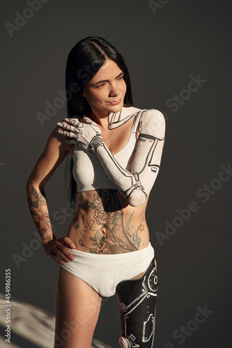 Vertical view of the tattooed female with cyborg pattern on her body posing at the studio on dark background. People and robot concept photo