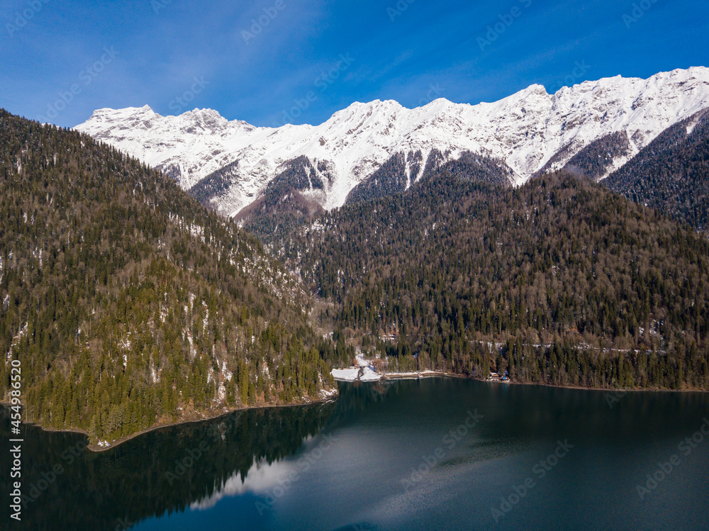 Aerial view of mountain glacial lake Ritsa in Abkhazia at winter season. Rocky mountain peaks covered with snow. Beautiful mountain landscape from drone. Abkhazia.