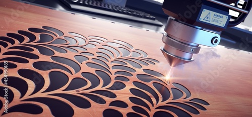 Laser cutter close up, cutting flower patterns on a wooden board.  photo