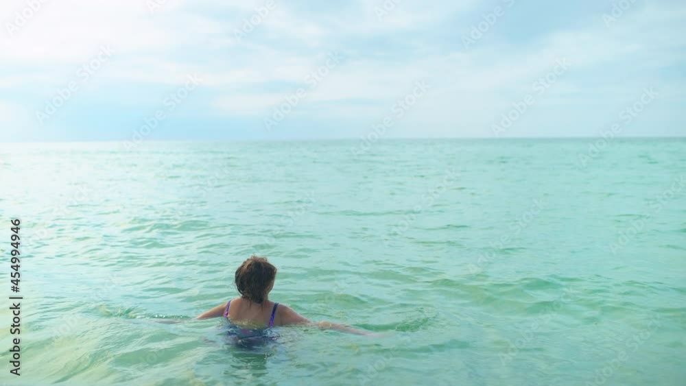 Young female woman in one piece swimsuit swimming in cold clear ocean turquoise water in Seaside, Florida Gulf of Mexico beach on panhandle in winter Young female woman in one piece swimsuit swimming in cold clear ocean turquoise water in Seaside, Florida Gulf of Mexico beach on panhandle in winter