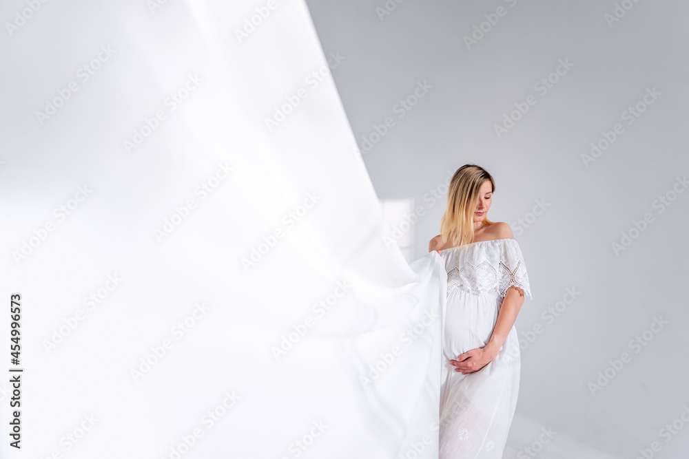 Pregnant woman holds white lightweight fabric in minimalist interior with light shadows from window Pregnant woman holds white lightweight fabric in minimalist interior with light shadows from window