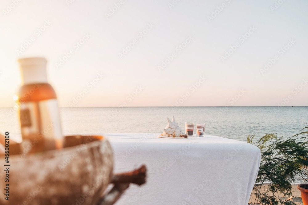 Obraz premium Massage white table by the sea at sunrise. There are pots of flowers near the table. Dawn sun. A jar of oil in front of the table without focus.
