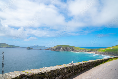 Bay surrounded by road and rock wall and steep dramatic coastal rock cliffs with flat green fields to the edge along Wild Atlantic Way tourist route.