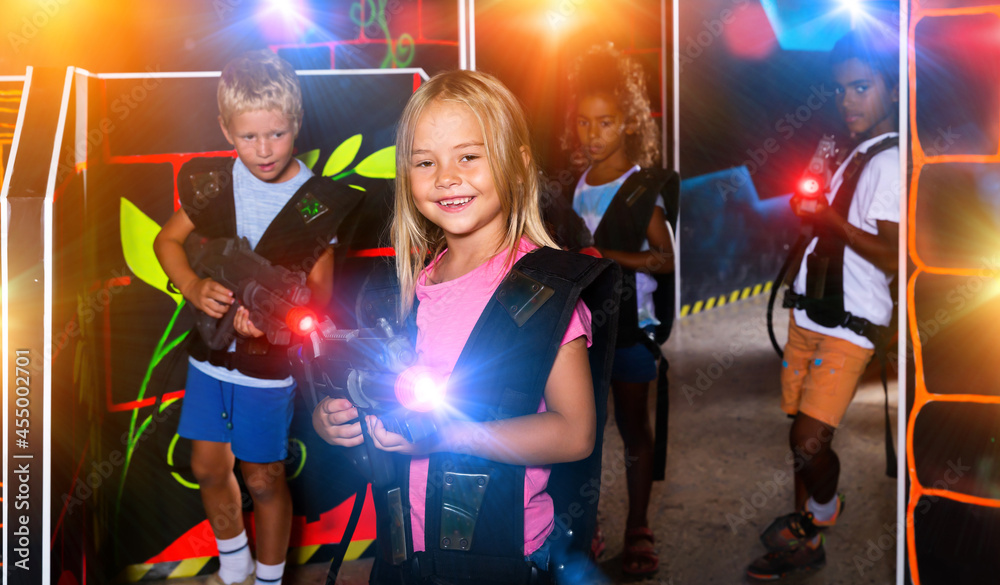 Fototapeta premium Smiling girl aiming laser gun at other players during lasertag game in dark room. High quality photo