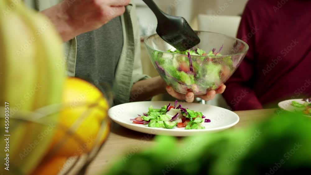An attractive man is putting salad on the plates 
