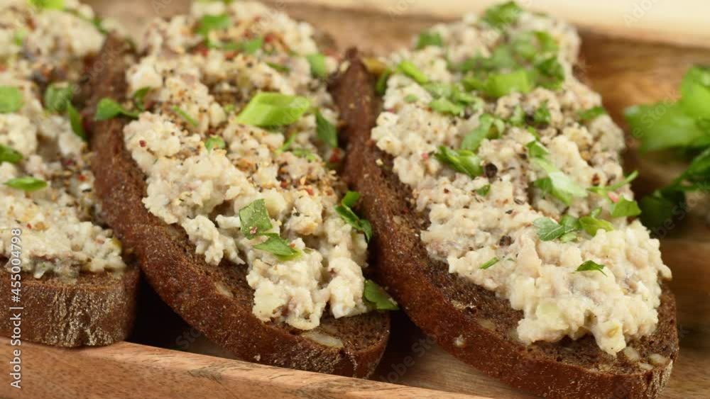 Israeli cuisine. Forshmak with parsley and spices on black rye bread close-up. National Jewish herring dish, middle eastern culture. Traditional snack vorschmack made of fish fillet rotating.