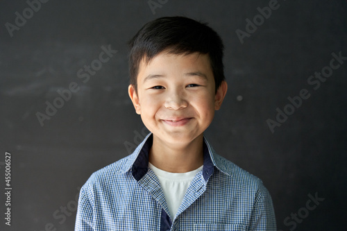Happy cute Asian kid boy school student looking at camera at blackboard background. Smiling ethnic child pupil posing in classroom. Junior elementary education. Back to school in Asia concept Portrait photo