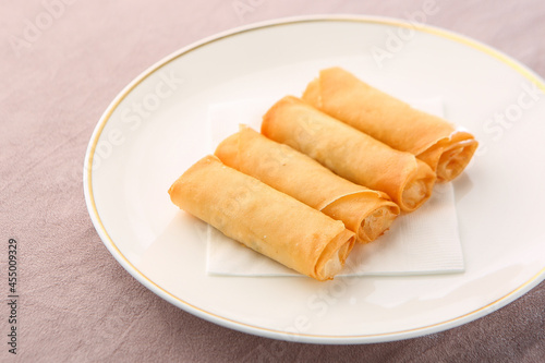 A bright background and four spring rolls on a white plate 밝은색 배경 그리고 흰색 접시에 담겨져 있는 춘권 4개