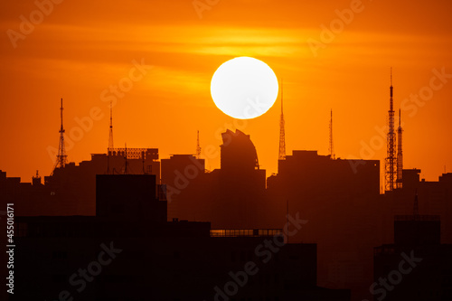 Por do Sol na grande cidade entre prédios e torres de transmissão à sombra com o grande Sol ao fundo