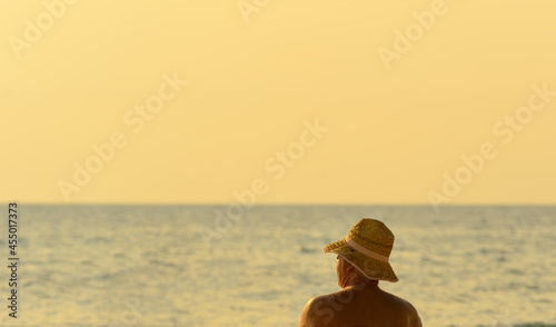 unrecognizable senior man wears straw hat sunbathing at sea beach photo