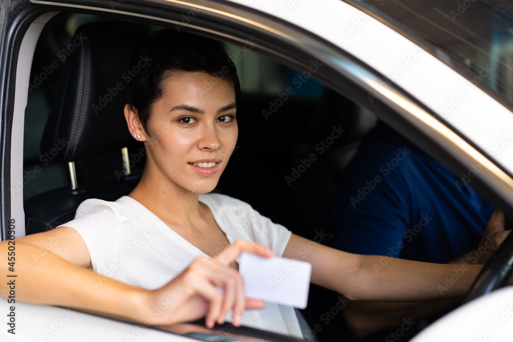 Confident young woman driver in car holding blank card mockup. Caucasian woman showing new driver's license