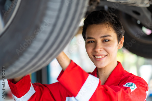 Empowering caucasian waman mechanic wearing red uniform working Under a Vehicle in a Car Service station. Expertise mechanic working in automobile repair garage. photo