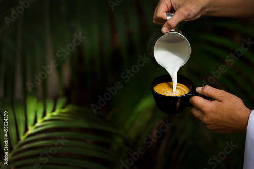 Barista pouring milk into coffee against tropical palms