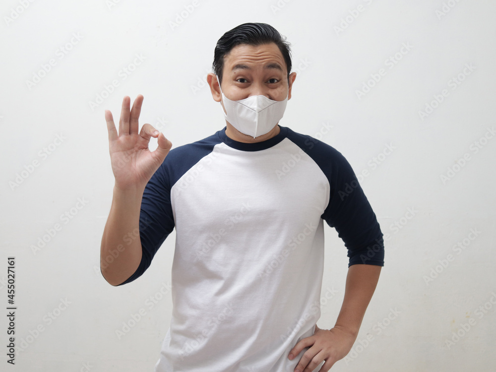 Asian man wearing protective mask shows OK sign gesture, good positive expression, dealing with new normal life caused by covid pandemic Asian man wearing protective mask shows OK sign gesture, good positive expression, dealing with new normal life caused by covid pandemic