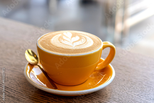 Cappuccino in yellow cap with latte art on a wooden table