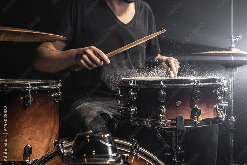 Fototapeta premium A male drummer plays snare drum with drumsticks in a dark room.