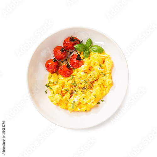 Creamy scrambled eggs for healthy breakfast served with baked cherry tomatoes and fresh basil leaves. top view