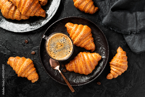 French croissants for breakfast. Freshly baked croissants with cup of coffee on black stone background. Tasty croissants. Top view