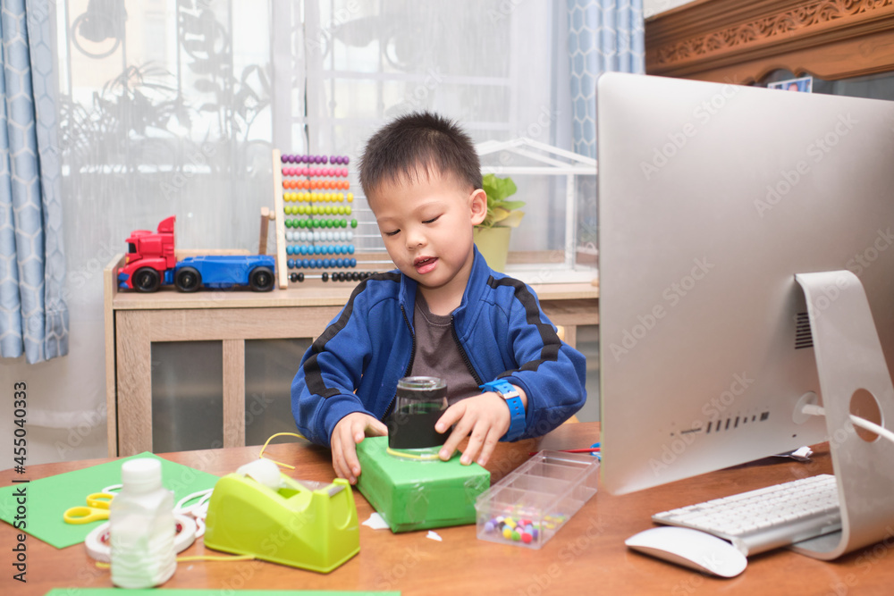 Asian little kid making art and craft project using computer alone during his online lesson at home, Kindergarten closed during the Covid-19 health crisis, Distance learning, homeschooling concept Asian little kid making art and craft project using computer alone during his online lesson at home, Kindergarten closed during the Covid-19 health crisis, Distance learning, homeschooling concept