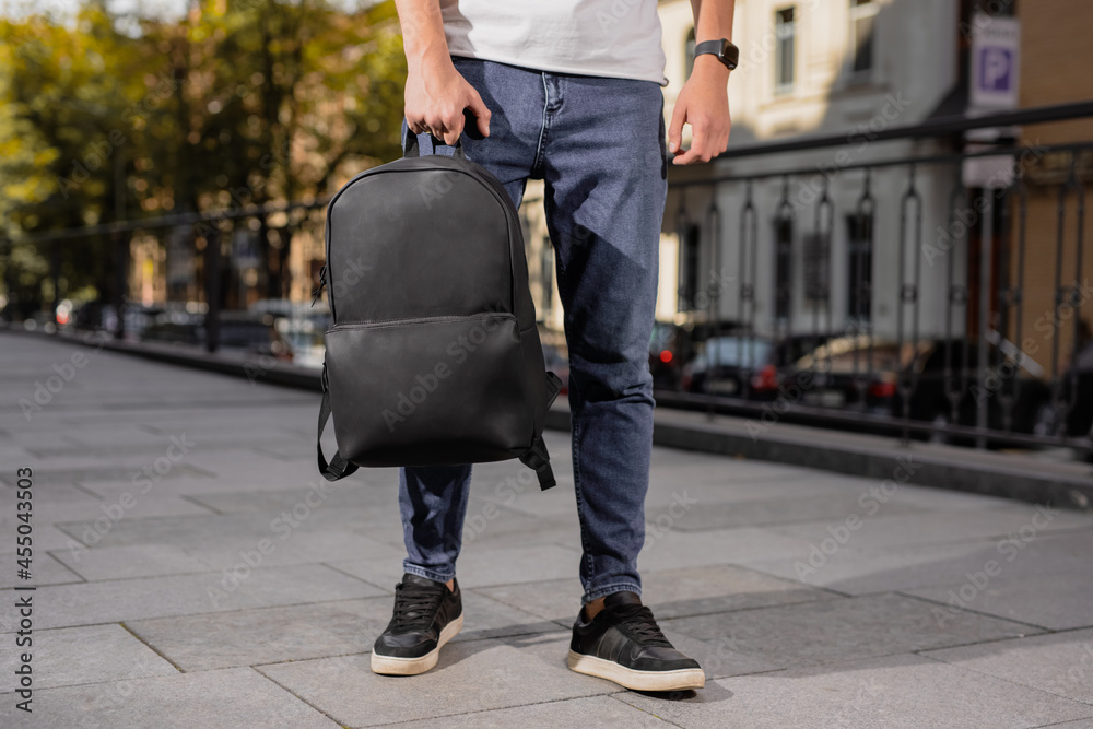 A black leather backpack holding male hand in city