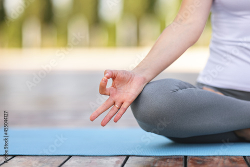 Cropped shot of female sitting on lotus pose on mat and meditating during yoga outdoor class