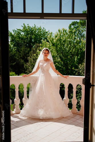 the bride in a white lace dress and a long veil stands on the terrace.