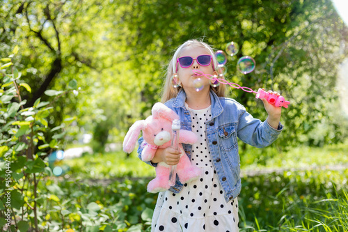 a happy little girl in summer with sunglasses inflates soap bubbles holds a toy in her hands. Background toning for instagram filter