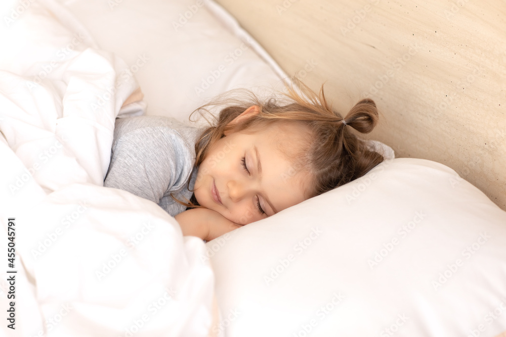 Little adorable child girl in grey pajamas closed eyes lying in bed sleeping on comfortable pillow and under white fluffy cotton blanket, good night sweet dreams Little adorable child girl in grey pajamas closed eyes lying in bed sleeping on comfortable pillow and under white fluffy cotton blanket, good night sweet dreams