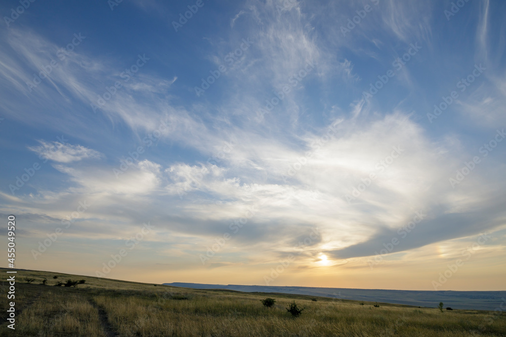Peaks of hills with steppe grass. Sunset sky and feather clouds.